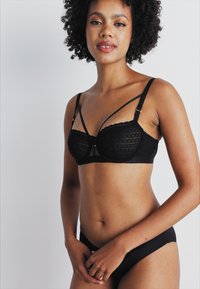 Black lace bra with structured cups, scalloped edges, and adjustable straps. Paired with matching black briefs. Smooth texture.