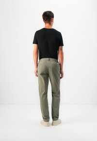 T-shirt nero a maniche corte abbinato a chinos verde oliva chiaro con tasche posteriori, indossato con sneakers beige, visto da dietro.