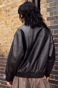 Giacca bomber in finta pelle nera con vita e polsini a coste, caratterizzata da una vestibilità ampia e una texture liscia, vista dal retro.