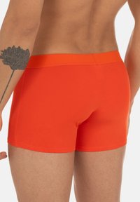 Boxer shorts in cotone rosso con una vestibilità aderente, dotati di una cintura liscia e un design senza cuciture per il massimo comfort. Tatuaggio visibile sul braccio.