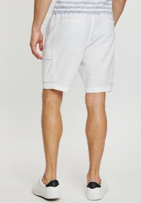 Shorts cargo blancos con dos bolsillos laterales y dobladillos enrollados, hechos de una tela ligera. Usados con zapatillas blancas que tienen un acento negro.