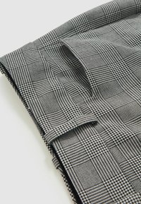 Trestăts frumos pliată cu un model negru și alb de houndstooth și pătrățele, evidențiind textura și țesătura detaliată pe un fundal deschis.