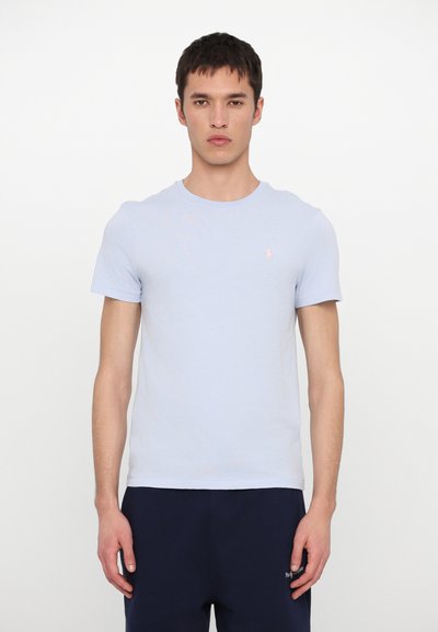 T-shirt en coton bleu clair avec un col rond, des manches courtes et un petit logo rose sur la poitrine gauche. Texture lisse.