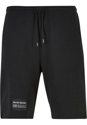 Schwarze Baumwollshorts mit elastischem Bund, verstellbaren Kordeln und einem seitlichen Label mit Pflegehinweisen und Markennamen.