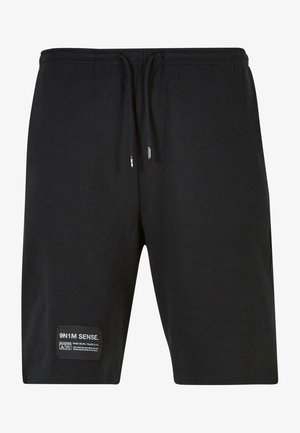 Mustast puuvillast lühikesed püksid elastse vöökoha, reguleeritavate paeltega ning küljepeal sildiga, millel on hooldusjuhised ja brändinimi.