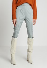 Světlé modré kalhoty na míru s bočními švy, spárované s bílými vysokými kozačkami. Oblečení doplňuje živý oranžový strukturovaný svetr.