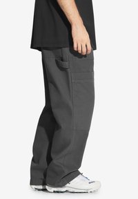 Szare spodnie cargo z bocznymi kieszeniami, luźny krój i solidny materiał. Noszone z białymi butami sportowymi z kolorowymi akcentami.