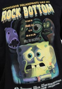 Camiseta negra con gráficos de dibujos animados coloridos de SpongeBob y criaturas, con texto en negrita. Destacada por su tela suave y su impresión vibrante.