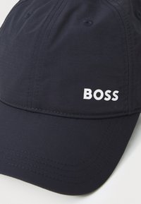 Casquette bleu marine en tissu texturé, avec une visière courbée et le logo blanc "BOSS" à l'avant, présentant des détails de couture visibles.