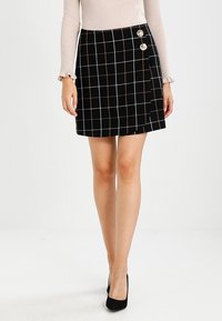 Sort skotskternet miniskirt med horisontale og vertikale linjer i hvid og brun, med to dekorative knapper på venstre side.