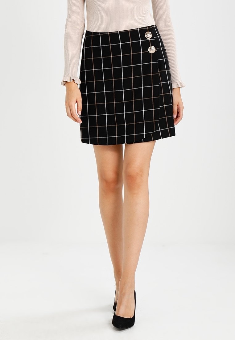 Sort skotskternet miniskirt med horisontale og vertikale linjer i hvid og brun, med to dekorative knapper på venstre side.