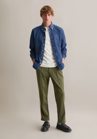 Donkerblauw denim overhemd, witte T-shirt eronder, groene sportbroek met zijstrepen en zwarte schoenen. Minimalistisch ontwerp en casual pasvorm.