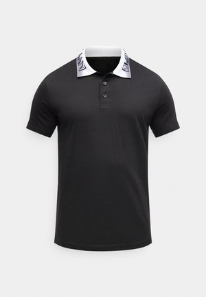 Polo de manga corta negro con cuello blanco que presenta texto negro y dos botones delanteros, mostrado sobre un fondo liso.
