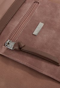 Rosenfarbige Geldbörse mit strukturiertem Wildlederfinish, ausgestattet mit einem silbernen Reißverschluss und einem Leder-Zugband sowie einem metallischen Markenschild.
