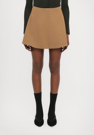 Jupe A-line marron, en tissu lisse, avec un ourlet net et sans coutures visibles, assortie à des chaussettes noires jusqu'à la cheville et des chaussures à bouts pointus.