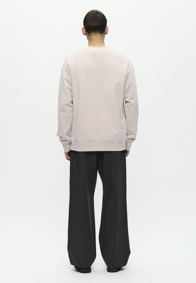 Helles graues Sweatshirt mit gerippter Textur, Rundhalsausschnitt und lässiger Passform, kombiniert mit dunklen, weiten Hosen.