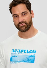 Weißes T-Shirt mit einem blauen Grafikdruck, der den Text "ACAPULCO" und ein Design eines Klippenspringers zeigt, umgeben von Palmen und Wellen.