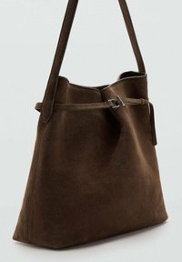 Bolso tote de ante marrón con una textura suave, apertura amplia y un detalle de cinturón. Cuenta con una sola correa para el hombro para su transporte.