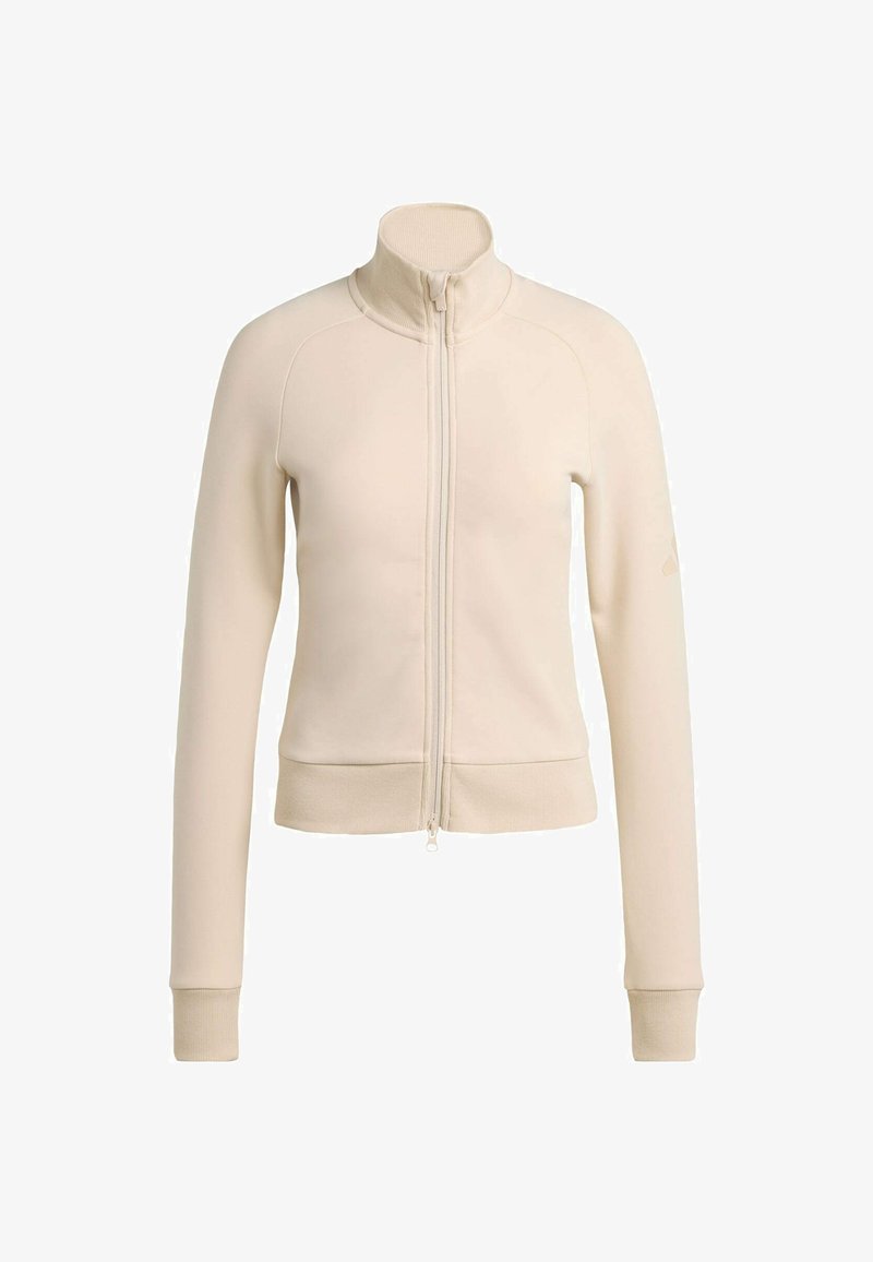 Giacca beige chiaro con cerniera in materiale morbido. Presenta un colletto alto, maniche lunghe, polsini a coste e vita aderente. Dettaglio logo discreto.