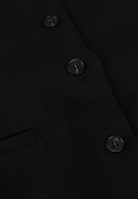 Tejido de chaqueta negra con una textura suave, que cuenta con cuatro botones negros y un pequeño bolsillo en el lado izquierdo.