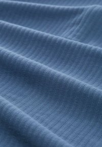 Světle modrá texturovaná tkanina s paralelními žebrovanými pruhy, měkká a mírně elastická, předvádějící jemné variace v barvě a hloubce.