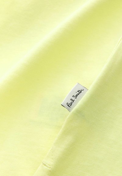 Tela de algodón amarilla con una textura suave, que presenta una pequeña etiqueta blanca con texto en negro que dice "Paul Smith."
