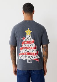 Dark gray T-shirt featuring a graphic of a Christmas tree with a yellow star, red ribbons, and skull accents, printed on the back.
