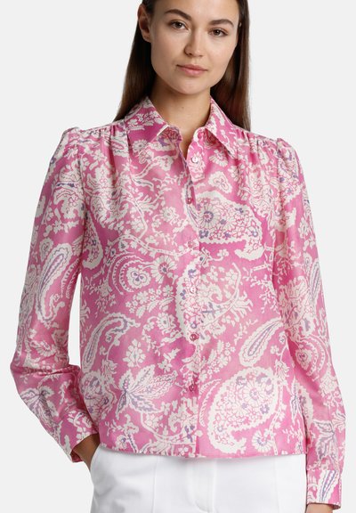 Blusa rosa a fantasia con maniche lunghe, chiusura frontale a bottoni e colletto classico. Presenta motivi floreali e paisley in bianco e lavanda.