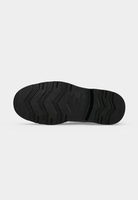 Semelle de chaussure en caoutchouc noir avec motifs de rainures en zigzag et nom de marque "GANT" embossé au centre du talon.
