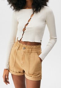 Gestreiftes weißes Langarmoberteil mit Knopfdetails, kombiniert mit beige Shorts mit Umschlägen, die einen elastischen Bund und vordere Taschen aufweisen.