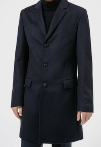 Abrigo largo azul marino de mezcla de lana con solapa con muesca, cierre de cinco botones, bolsillos laterales y corte recto. Tejido texturizado que proporciona calidez.