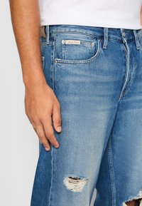 Svijetloplave traper šorts hlače s istrošenim detaljima, s malim raspuklinom na lijevoj nozi i Calvin Klein logotipom na stražnjem džepu.