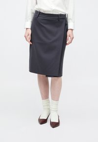 Pelēks zīmulis svārks ar gludu tekstūru, divām priekšējām kabatām un jostas cilpām, kopā ar baltām zeķēm un brūnām kurpēm ar smailiem purngaliem.