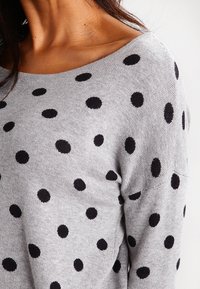 Grå tröja med svarta prickar. Har en vid halsringning, mjuk textur och ribbat detaljer på ärmar och nederkant.