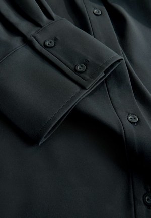 Schwarzes Hemd mit Knopfleiste und glatter, matter Textur. Mit Manschettenknöpfen und einem klaren, maßgeschneiderten Design, das auf Einfachheit setzt.