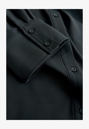 Schwarzes Hemd mit Knopfleiste und glatter, matter Textur. Mit Manschettenknöpfen und einem klaren, maßgeschneiderten Design, das auf Einfachheit setzt.