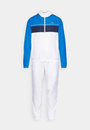 Chándal en blanco con detalles en azul, que incluye una chaqueta con cremallera y pantalones con cintura elástica. El material es ligero y tiene una textura suave.