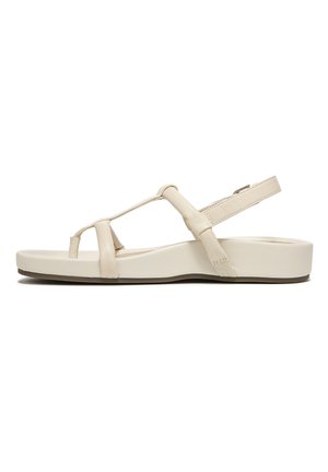 Beige sandal with flat sole, crossover straps, and adjustable ankle strap. Made of smooth synthetic material for comfort and durability.