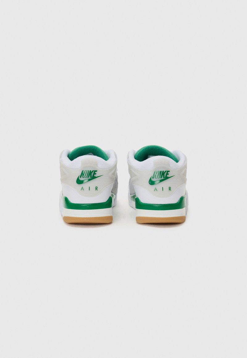Baskets Nike blanches avec des accents verts, dotées d'un col de cheville rembourré, d'une semelle extérieure en gomme et d'un branding "Nike Air" proéminent à l'arrière.