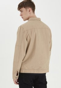 Lyse beige jakke laget av bomull, med en avslappet passform, knappeermer og sidelommer. Enkelt design uten synlige mønstre eller detaljer.