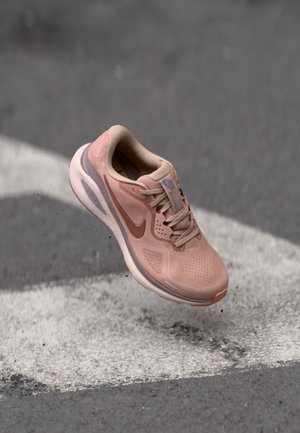 En enkel lyserød Nike løbesko, der svæver over asfaltvej med hvid malet linje, set fra oven og fronten.