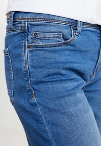 Blue denim jeans featuring a classic four-pocket design, contrast stitching, and a smooth texture with a slight fading effect.