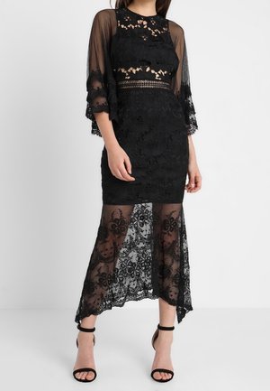 Robe en dentelle noire avec une doublure courte et des manches en dentelle transparentes et fluides. Présente des motifs floraux, un corsage ajusté et un ourlet asymétrique.