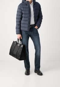 Padded navy jacket with a hood, paired with blue jeans and black leather boots. Holding a structured black tote bag with a subtle pattern.