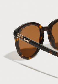 Skilpadde-sunglasses med runde rammer, brune linser, gulldetaljerte armer og logo på brillestangen.