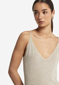 Beżowy top bez rękawów z głębokim dekoltem w serek, wykonany z miękkiego materiału. Posiada cienkie ramiączka i luźny krój.