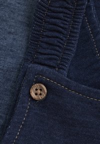 Donkerblauwe denimstof met een ribbelstructuur, voorzien van een houten knop met vier gaten en contrasterende gele stiksels langs de rand.