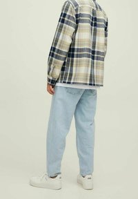 Chemise en flanelle à carreaux bleus marine, beige et blancs ; associée à un jean baggy bleu clair et des baskets blanches avec des détails de branding subtils.