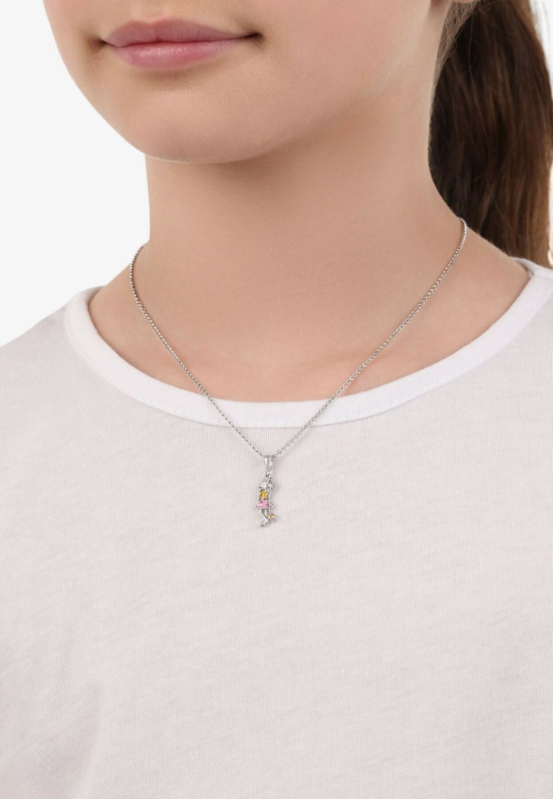 Silverhalsband med en hängande berlock som har färgglada ädelstenar, bärs över en vit T-shirt med rundad halsringning.