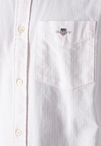 Camicia a righe rosa chiaro realizzata in tessuto con una texture liscia, dotata di una tasca sul petto sinistro e di un piccolo logo ricamato.